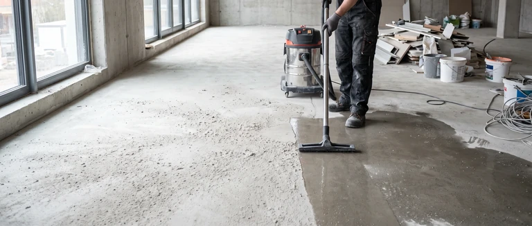 Symbolbild: Baustaub wird mit einem Industriesauger von einem Rohbauboden entfernt